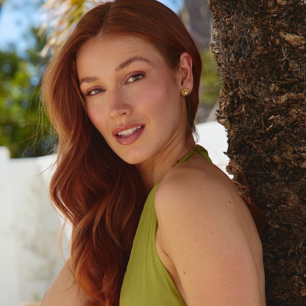 Golden Sunflower Stud Earrings, worn on an ear of a model in a green halter top